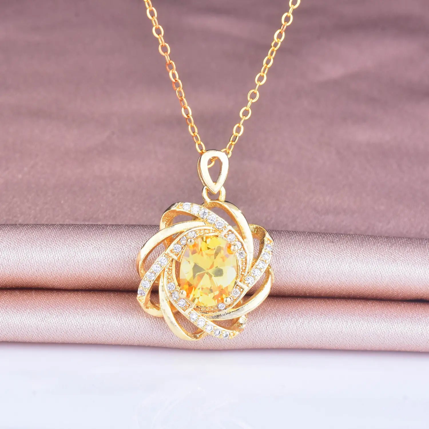 Collier pendentif moulin à vent en citrine doré comportant une pierre ovale centrale en citrine entourée de bandes dorées tourbillonnantes et sertie de petits diamants transparents, accessoire en pierre de naissance dorée.