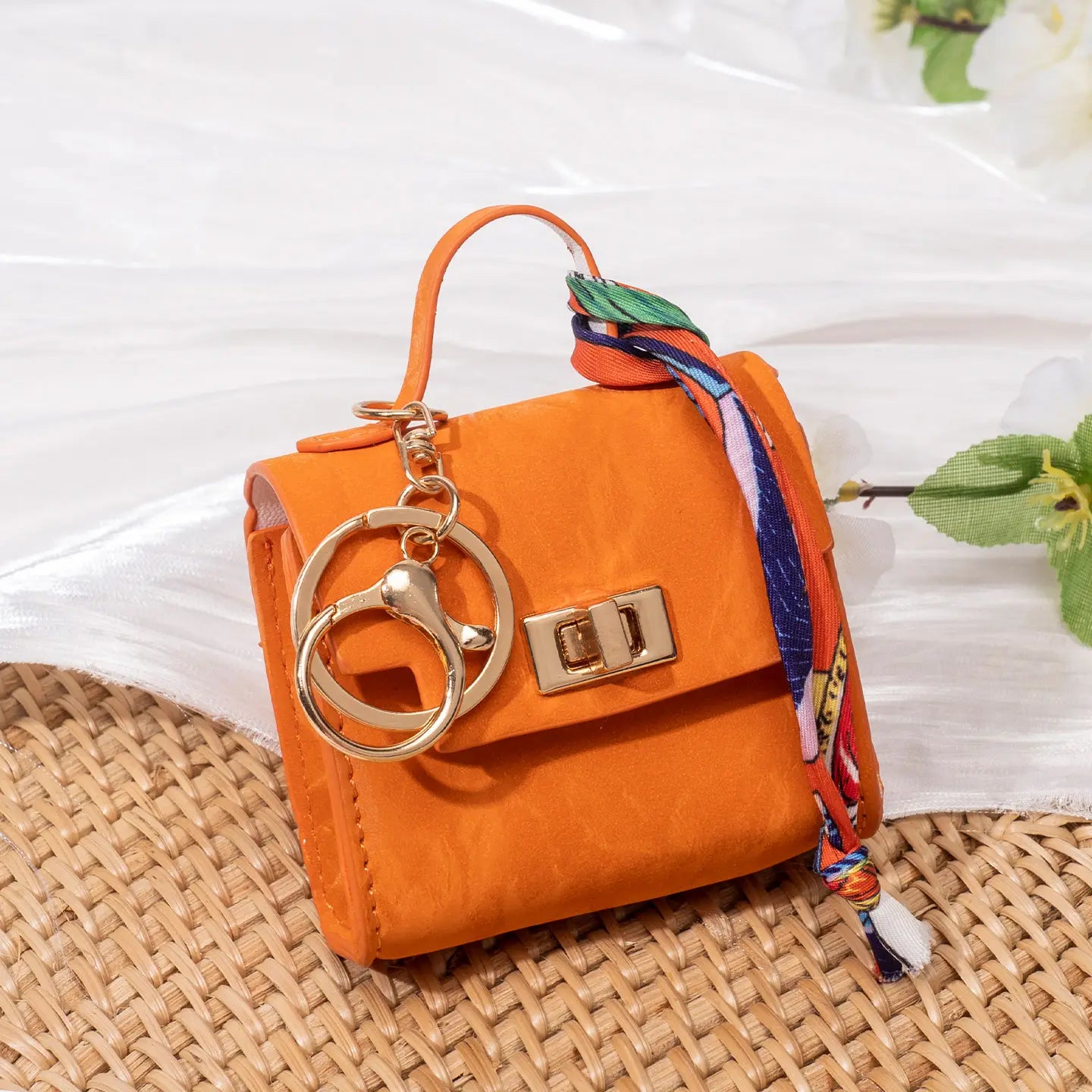 Vibrant orange miniature handbag keychain with gold-tone hardware and a colorful silk scarf tied around its handle.