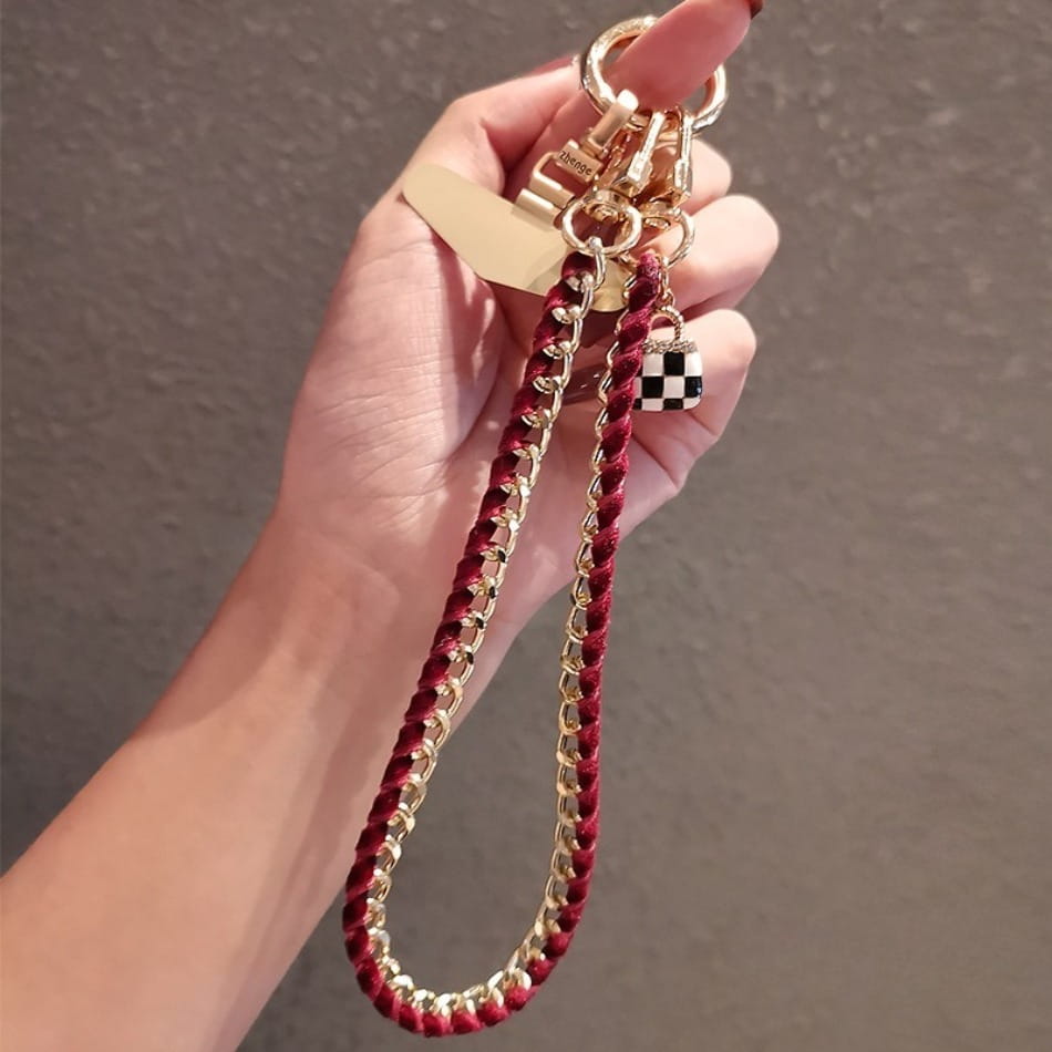 Handy-Handgelenkriemen aus goldfarbener Kette als Anti-Lost-Handylanyard, mit einer goldfarbenen Kette, bordeauxrotem geflochtenem Kord und einem schwarz-weiß karierten Schloss-Anhänger.