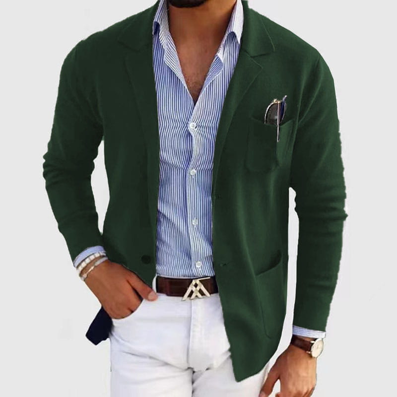 Chaqueta tipo blazer verde oscuro, de ajuste entallado, para hombre, con tejido de punto texturizado y solapas tipo púa, usada abierta sobre una camisa abotonada a rayas azul y blanca como chaqueta de traje formal.