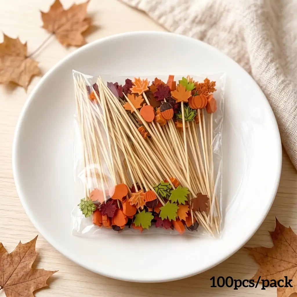 A pack of 100 bamboo food skewers each topped with colorful autumn-themed foam decorations in shades of orange green and brown.