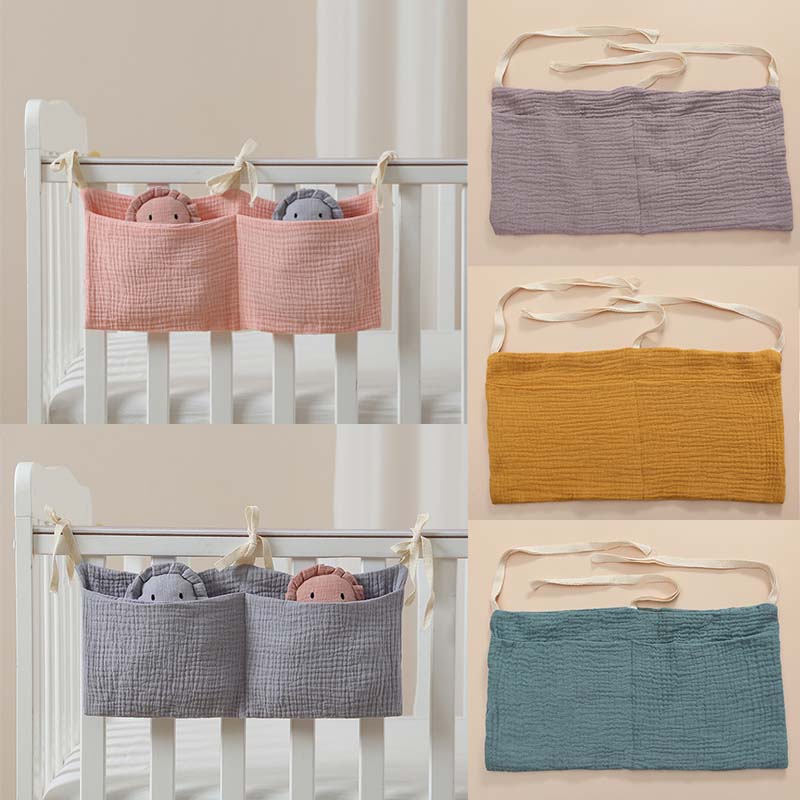 淡いパステルカラーのコットン・ミュスリン製ベビーベッド収納バッグで、2つのポケットと布紐の留め具付き。ベッドサイドのオーガナイザーとして設計されています。