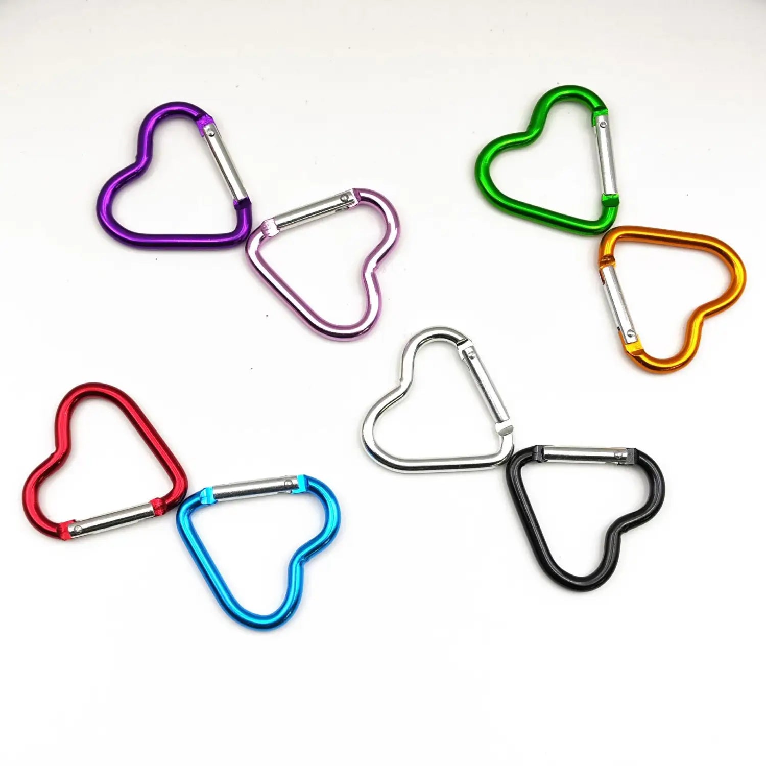 Set aus herzförmigen Karabinerhaken-Schlüsselanhängern mit farbenfrohen metallischen Karabinern in Violett, Grün, Rot, Blau, Silber und Schwarz.