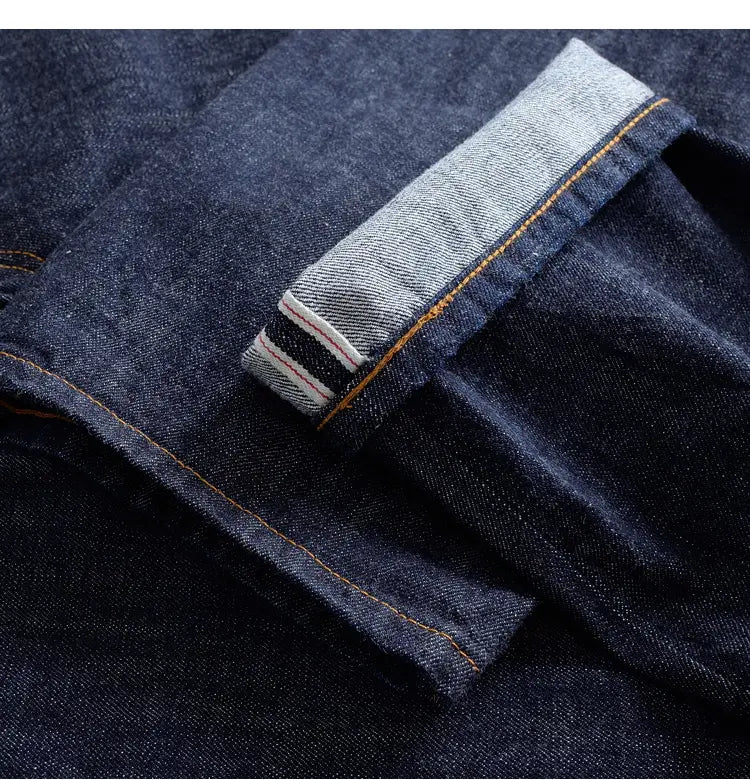 Heavyweight red selvedge denim jeans in dark blue with rolled cuffs revealing lighter inner fabric and distinctive striped stitching.