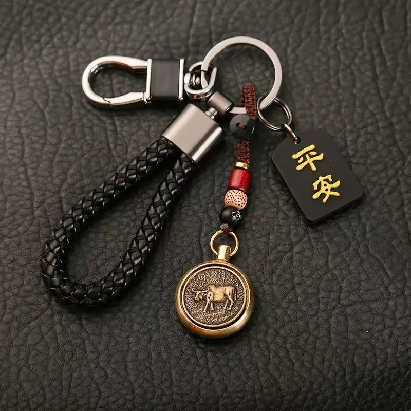 ブロンズの「牛」メダリオン、赤と黒のビーズ、金色の漢字が刻まれた黒いタグを備えた黒の編みレザー製キーチェーン（中国の干支をモチーフにした編みレザー製ラッキーペンダント）。