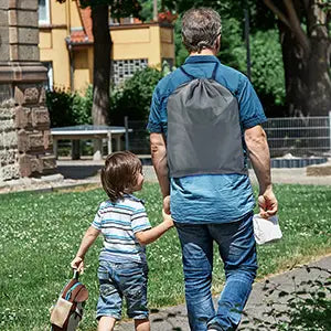 灰色の巾着式リュックサックを着用した子どもとともに後ろ姿から示されている男性であり、便利な携帯使用のための子ども用旅行用エアマットレスの自動インフレータブル・カーベッドを際立たせています。