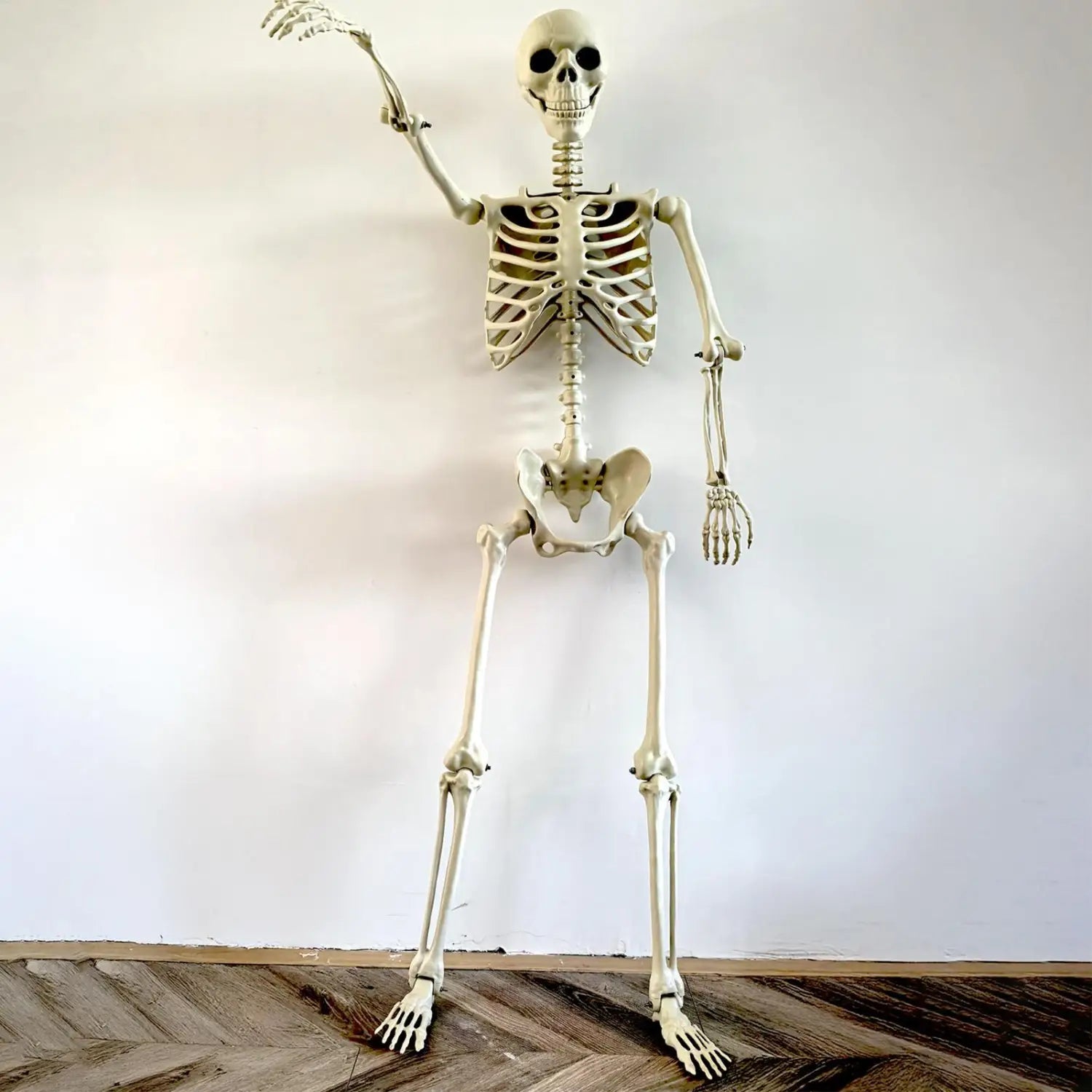 un esqueleto de Halloween de plástico color marfil pálido de tamaño completo, con extremidades articuladas y una mano en movimiento, diseñado como decoración posable para jardín en ambientes de casa encantada.