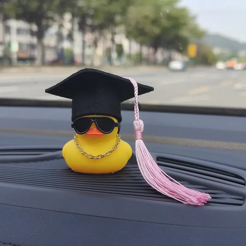 graduation rubber duck car dashboard ornament features a yellow rubber duck wearing a black graduation cap with a pink tassel sunglasses and a gold chain.