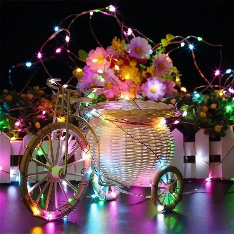 un panier décoratif de tricycle en osier garni de fleurs artificielles colorées, enveloppé de guirlandes lumineuses à DEL en fil de cuivre lumineux, vu de face