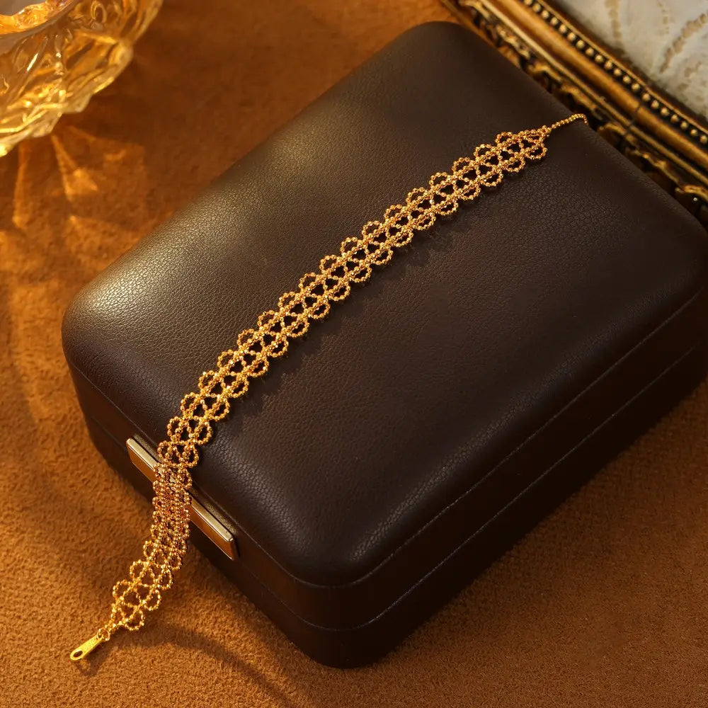 A delicate gold-toned metal lace bracelet featuring an intricate repeating floral pattern with a secure clasp and adjustable design for fashion jewelry.