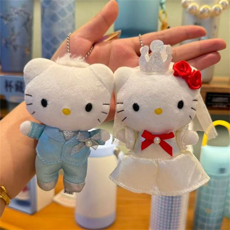 porte-clés en peluche couple de mariage Hello Kitty, représentant deux porte-clés en peluche blancs habillés d’un costume bleu clair avec des accents argentés, et d’une robe de mariage blanche avec ruban rouge, broche en perles et couronne en dentelle.