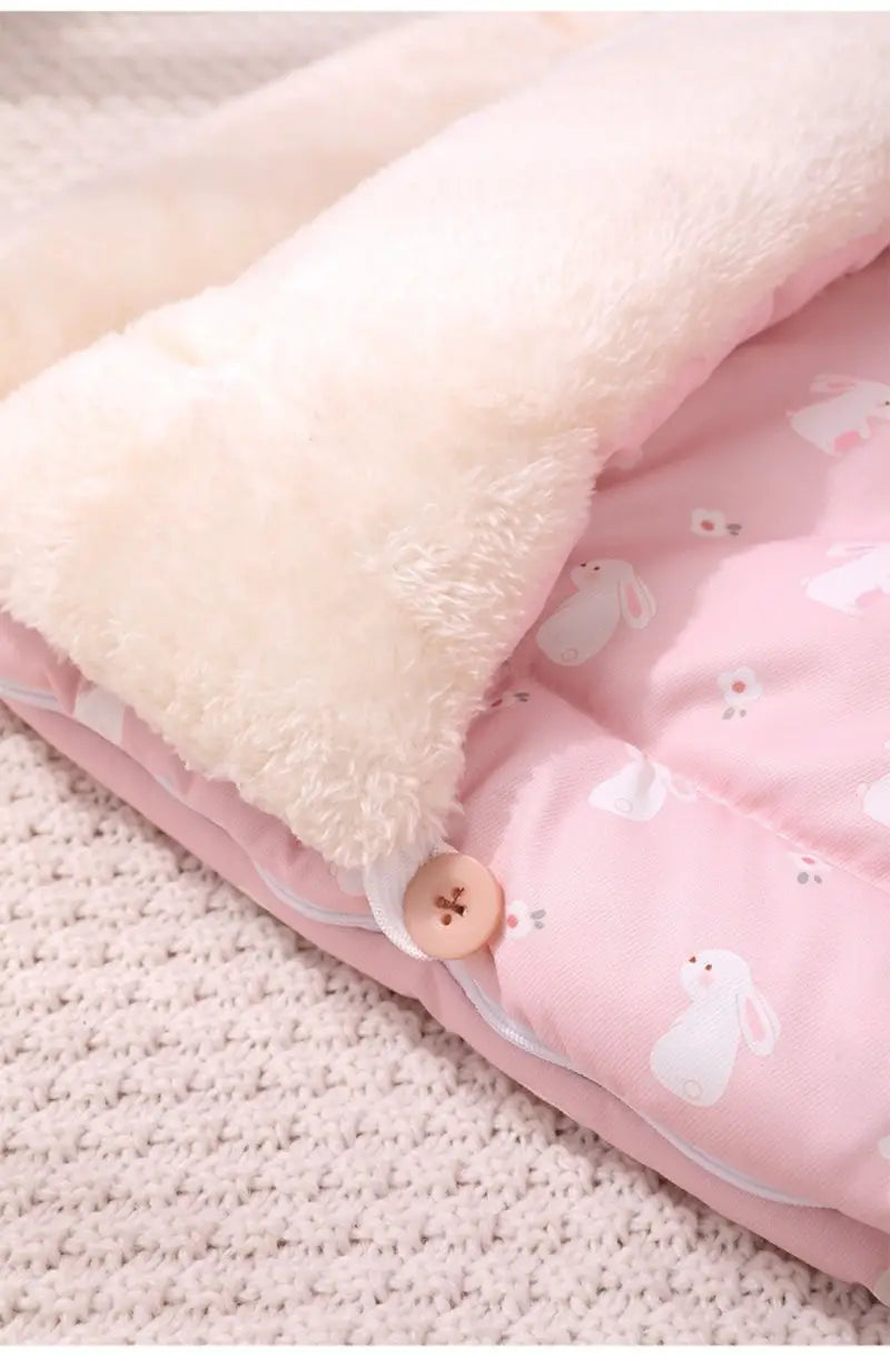 Cama acolchada para gato rosa con liebre durmiendo, bolsa de dormir que presenta una colcha rosa con estampado de conejito y un interior de forro polar color crema, con cierre de botón de madera