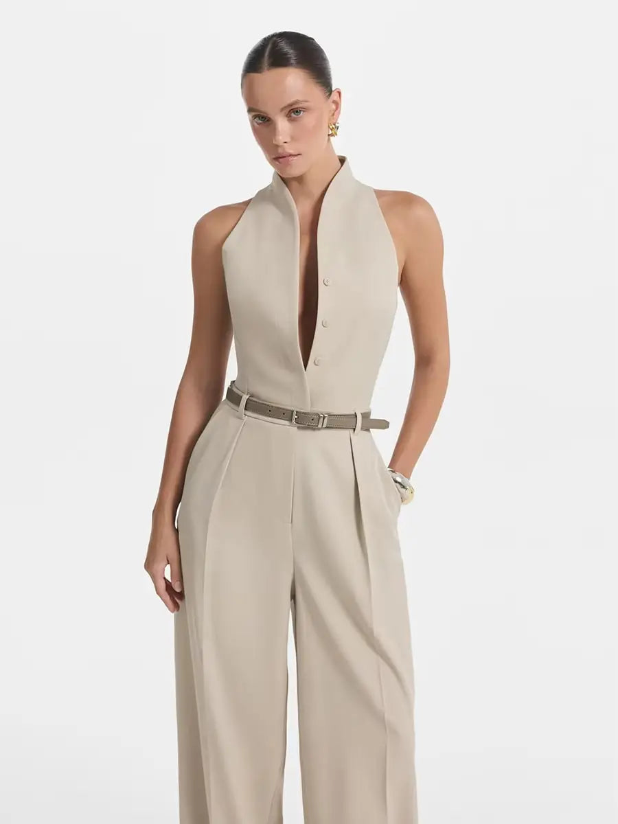 Une combinaison beige à col halter et jambes larges, avec un design sans manches, un détail de fermeture boutonnée à l’avant et un pantalon à jambes larges taille haute.