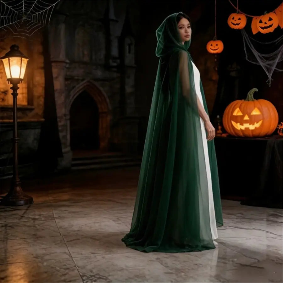 a flowing dark green velvet ghost costume hooded cloak with sheer inner lining worn by a model in a halloween-themed setting