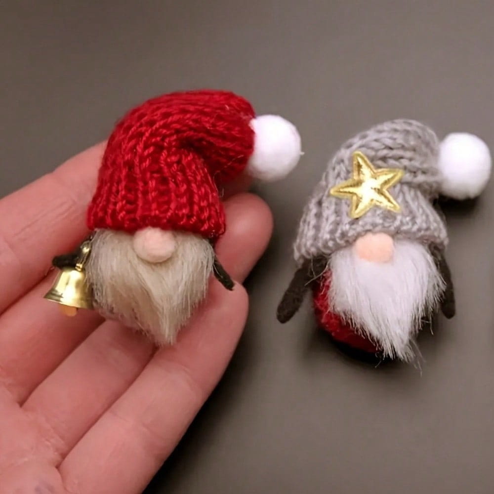 Vorderansicht eines roten, gestrickten Weihnachtsmann-Mützen-Gnom-Anhängers mit weißem Pompon und einer kleinen Mini-Glocke aus goldenem Material neben einem grauen, mit Sternen verzierten Strickmützen-Gnom mit flauschigem weißem Bart, der Mini-Glockenanhänger für Bastelarbeiten DIY trägt.