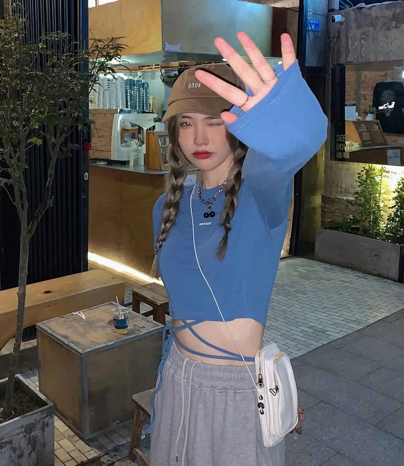 Weiße Umhängetasche mit schwarzen Reißverschluss-Ziehgriffen und kleinem Logodetail, kombiniert mit einem Damen-Langarm-Crisscross-Crop-Top in Weiß.