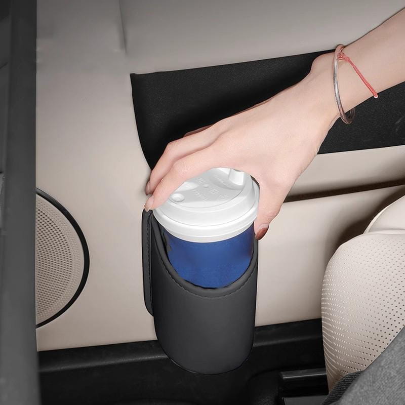 Portavasos de silicona negra que sujeta firmemente una taza de café desechable azul con tapa blanca, fijada a un organizador para asiento de coche y portavasos.