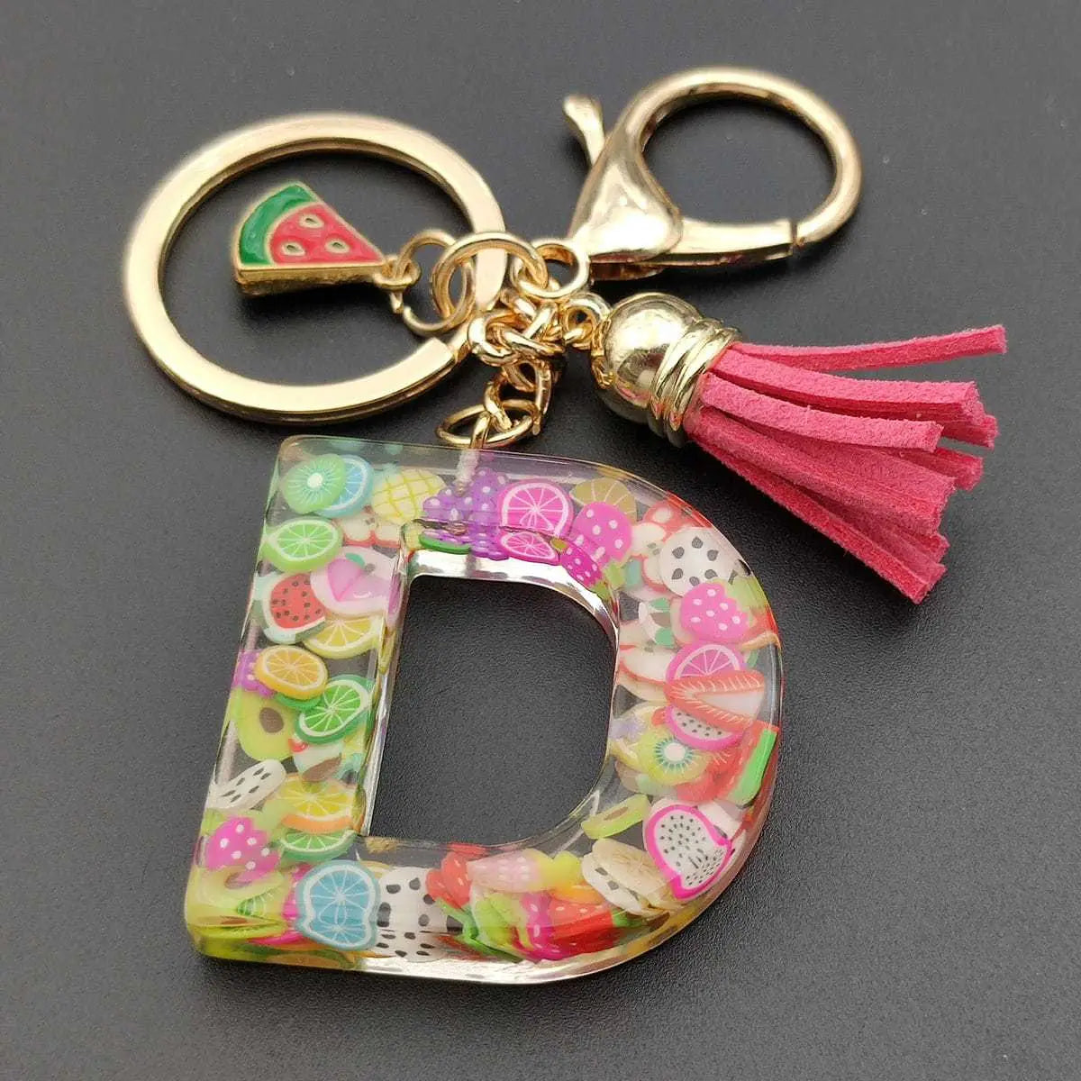 Clear resin letter d keychain with colorful fruit slice confetti, gold-tone metal clasp and ring, and pink suede tassel from fruit letter resin keychain initial alphabet key ring collection.
