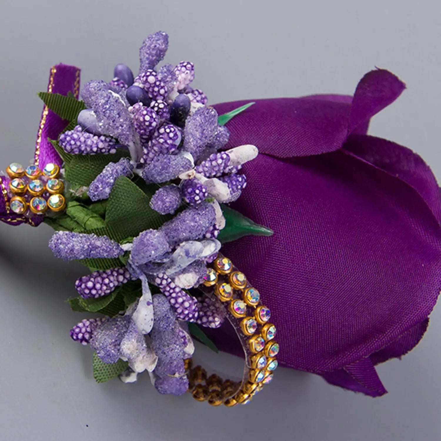 Purple floral wrist corsage featuring glittery lavender blossoms green fabric leaves and gold rhinestone accents for blue wedding boutonniere artificial silk rose corsage.
