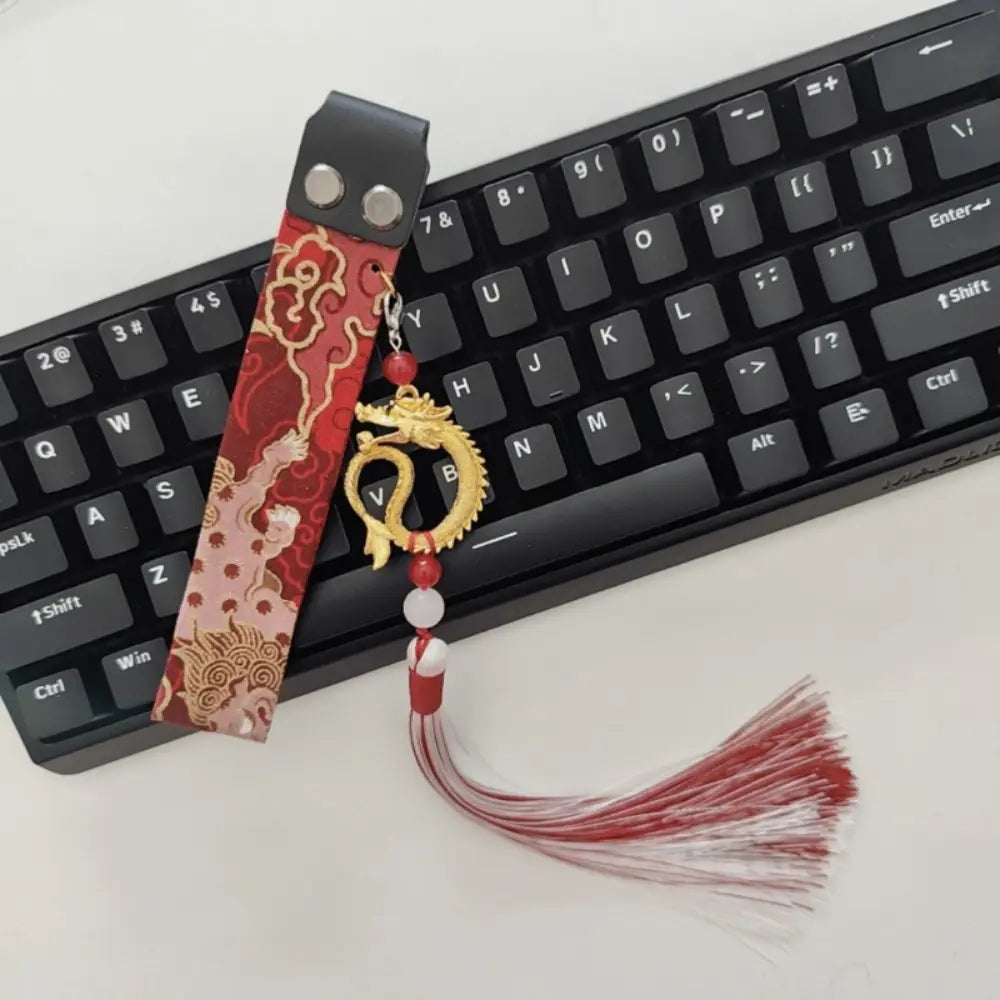 Sangle personnalisée pour le modèle Ribbon Dragon du clavier Wooting, comprenant une broderie sur le thème du dragon rouge et or avec des motifs de nuages, une languette en cuir noir, des perles rouges, une perle de type jade blanc et un pompon assorti.