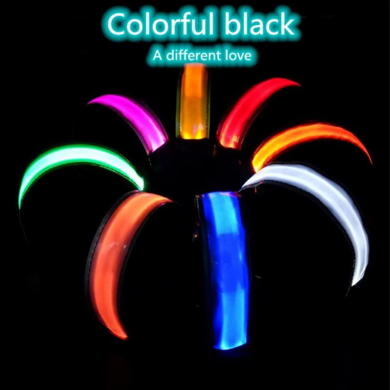 Una flor luminosa LED multicolor que se enciende, con pétalos vibrantes de color rosa, rojo, verde, naranja y azul, que irradian desde un tallo central negro, como parte de un brazalete de seguridad LED recargable por USB para correr