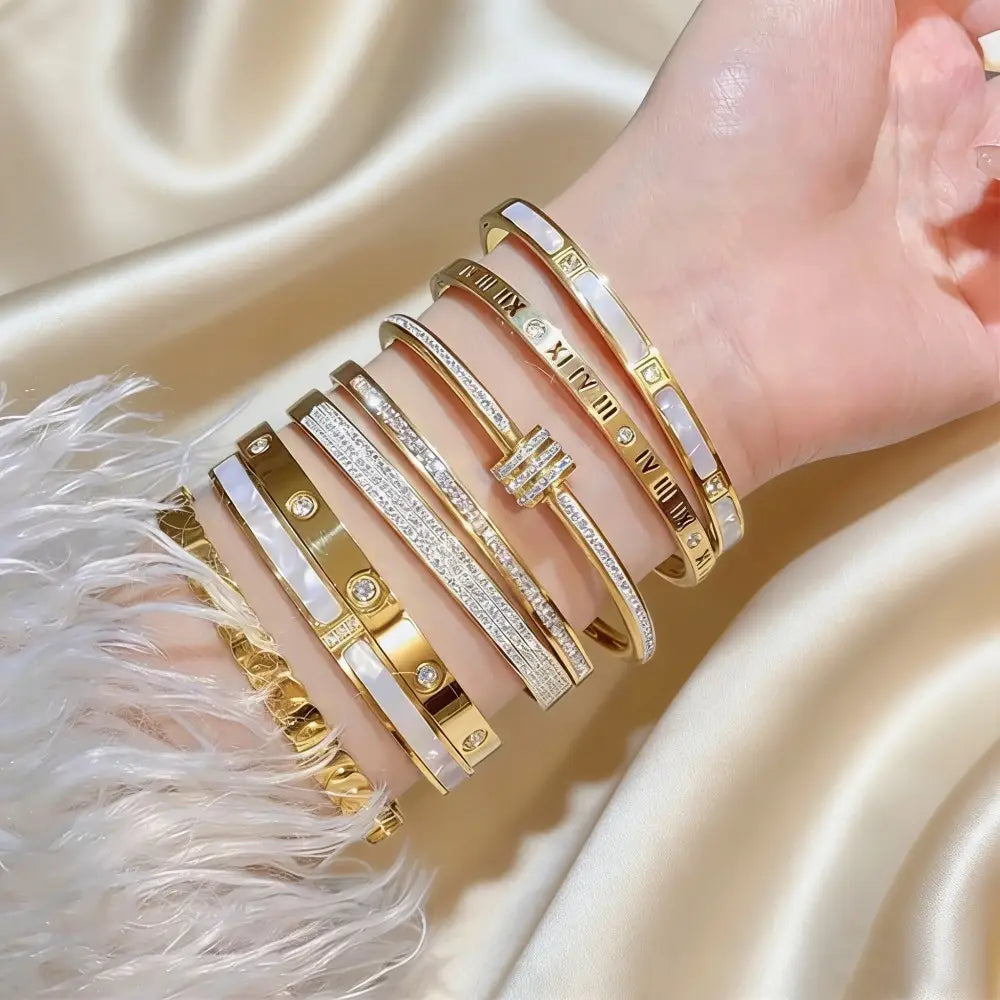 A collection of elegant stainless steel gold-toned roman numeral bangle bracelets for women featuring intricate designs with diamonds and mother-of-pearl accents.