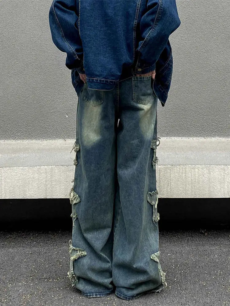 Jeans en denim délavé et déchiré baggy style y2k présentant une coupe très ample (wide-leg) et des détails déchirés effilochés sur les côtés et les jambes.