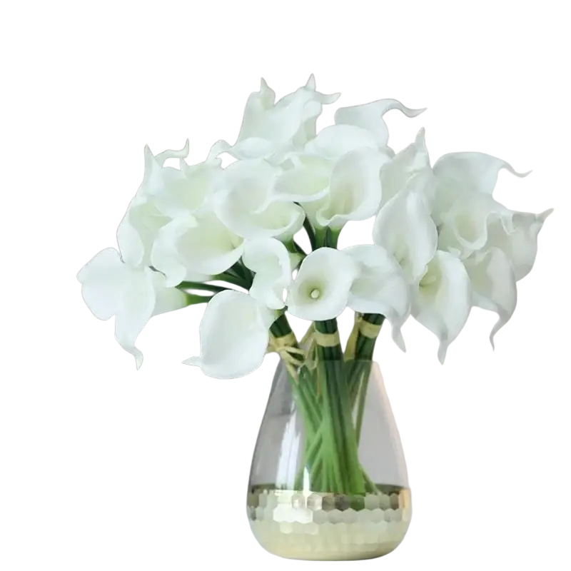 A bouquet of white calla lily simulation flowers arranged in a clear glass vase with a gold hammered base