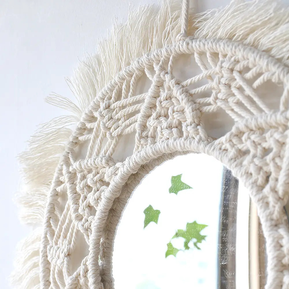 A cream-colored boho macrame wall mirror with an oval opening and tassel fringe ideal for living room home decor.