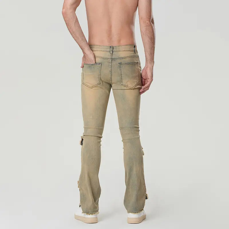 Une paire de jeans empilés déchirés pour hommes en denim olive délavé, à coupe slim, avec une coupe de jambe évasée, et des détails de fermeture éclair décoratifs sur les bas de jambes.