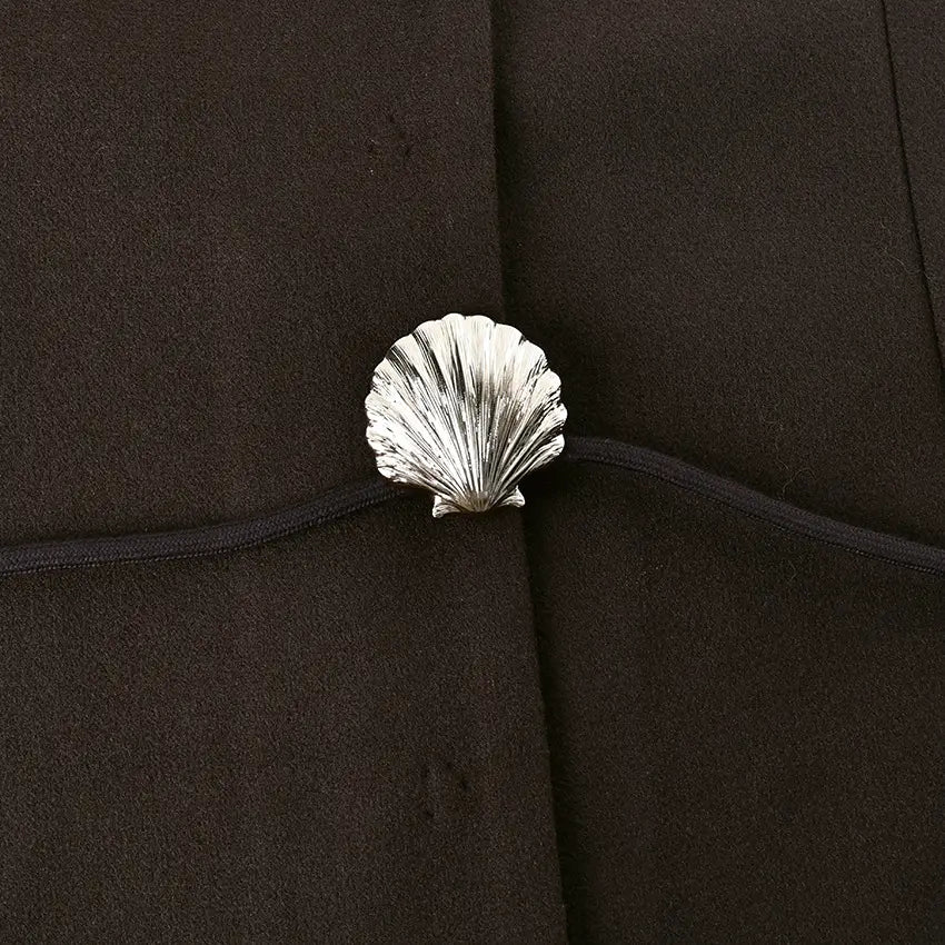 silver seashell-shaped button with detailed ridges attached to dark fabric of brown wool belted coat winter jacket