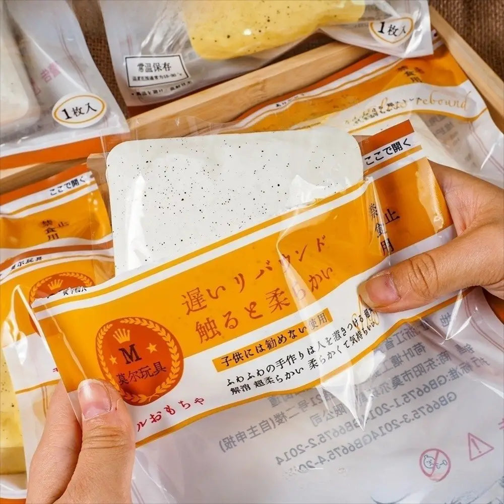 eine transparente Plastikhülle mit weißem gesprenkeltem Silikon-Spielteig mit orangefarbenem Etikett und japanischem Text neben einem Polyester-Acryl-Winterschal