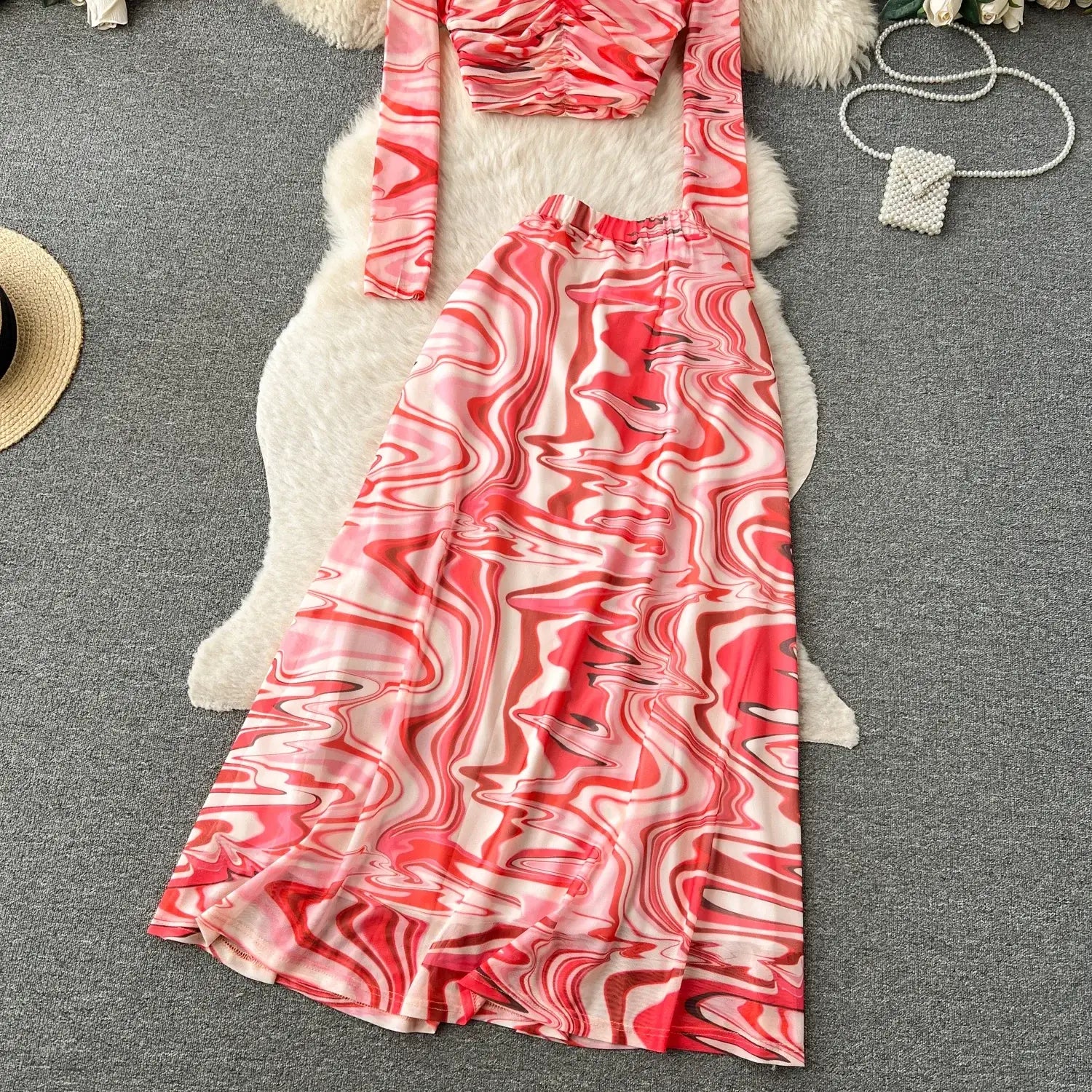 a flowing two-piece mesh skirt set with an elastic closure featuring a long-sleeved top and matching skirt in a red and white abstract marble print crafted from smooth shiny fabric.