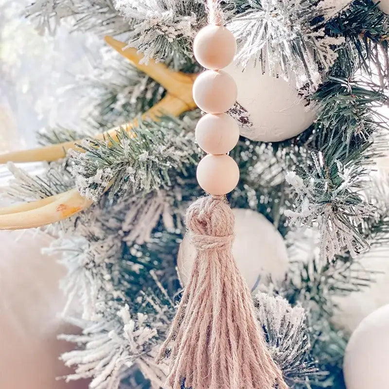 Ein zarter beigefarbener hölzerner Perlengirlanden-Tassel-Anhänger aus Holz, der anmutig von einem beschlagenen Weihnachtsbaum hängt.