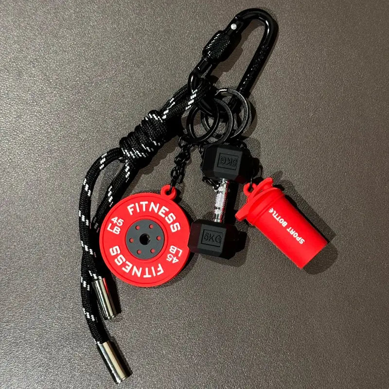 Un porte-clés de fitness rouge et noir comprenant un disque de poids circulaire, une mini-haltère et une breloque de bouteille shaker, conçu comme accessoire pour sac de sport.