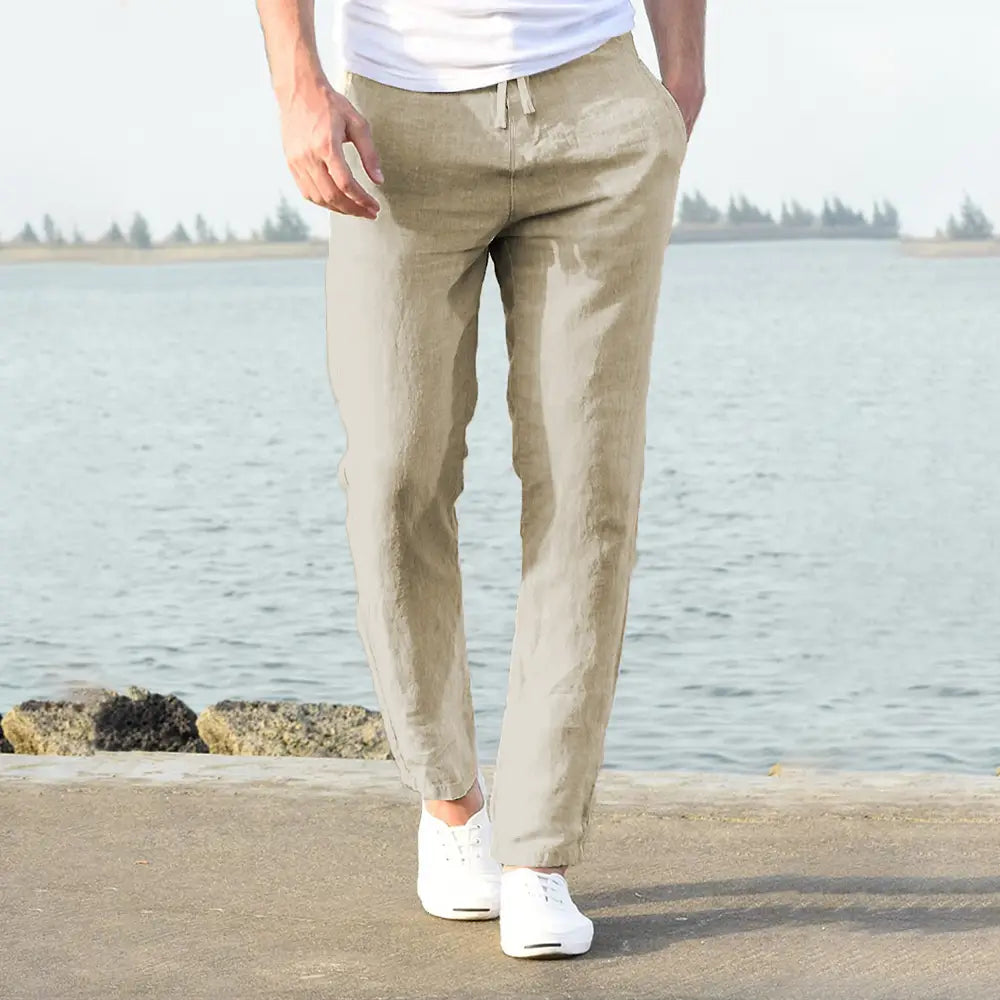Beige cotton linen trousers with a drawstring waist and tapered legs designed as breathable casual pants for men.