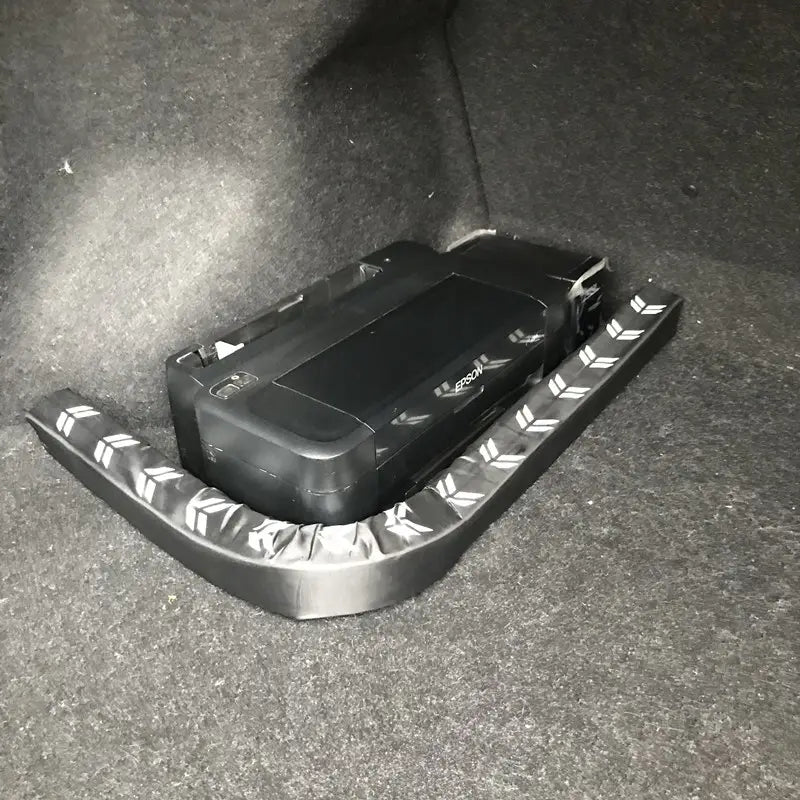 Impresora Epson negra apoyada sobre un organizador flexible para el maletero del coche y una varilla de almacenamiento fabricados con material metálico texturizado, con bordes elevados y agarre con patrón de rombos.
