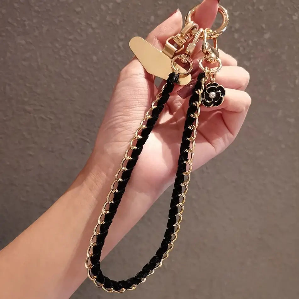 Schwarzer geflochtener Kord-Handy-Handgelenkriemen mit goldfarbenen Metall-Kettengliedern und einem dekorativen schwarzen Blumenanhänger zur Verwendung als Anti-Lost-Handylanyard.