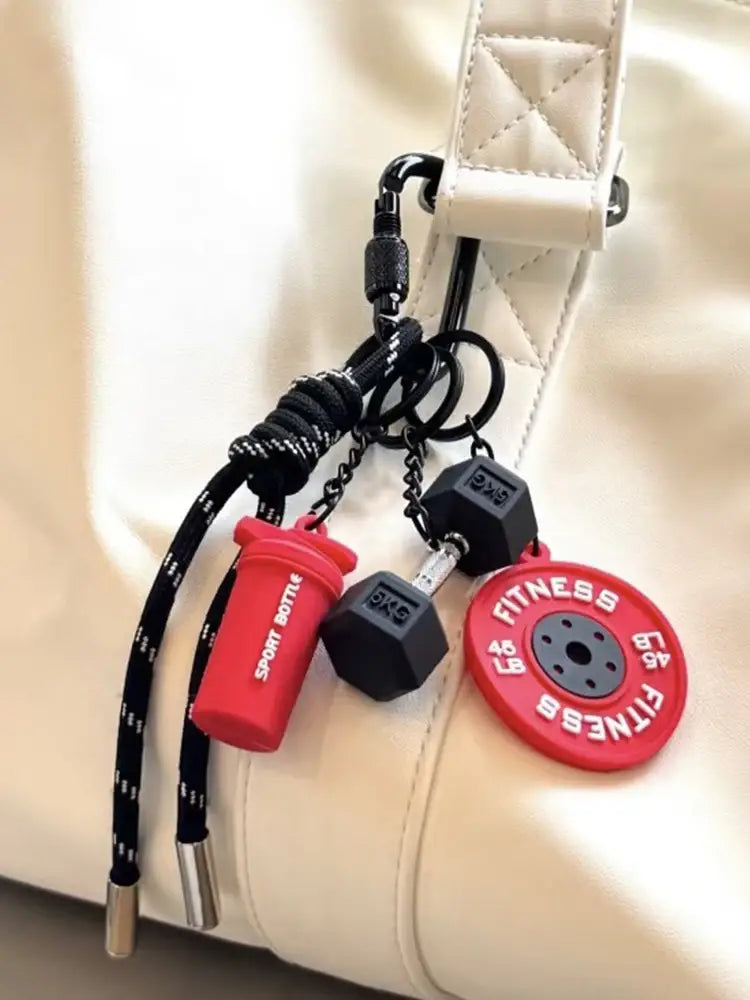 Porte-clés de musculation rouge et noir comprenant des breloques en silicone en forme d’haltère, de poids et de bouteille shaker, en tant qu’accessoire de cadeau pour l’entraînement.