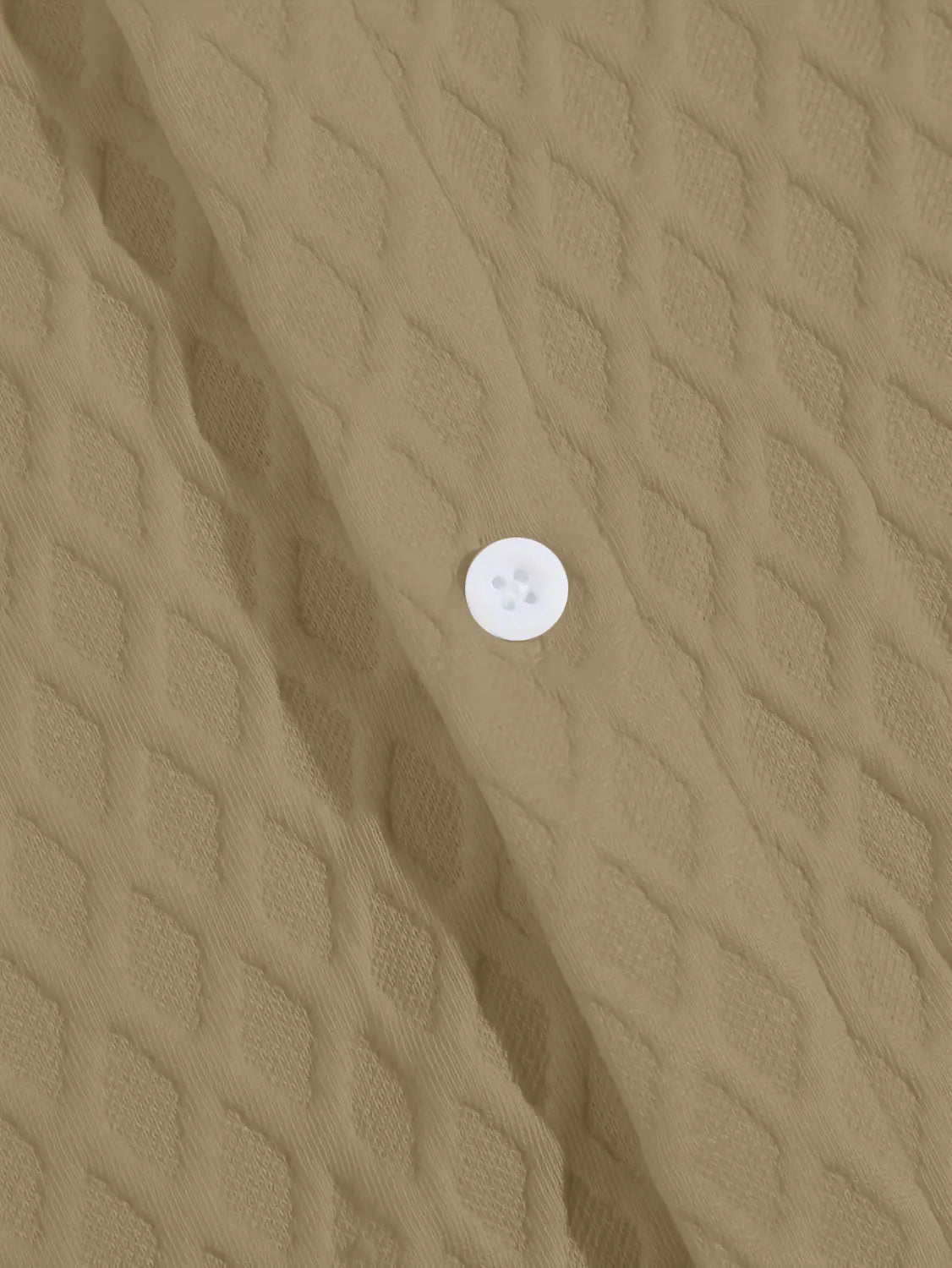 Un bouton blanc à quatre trous sur un tissu beige texturé en maille diamant du haut gris en maille diamant à manches courtes.