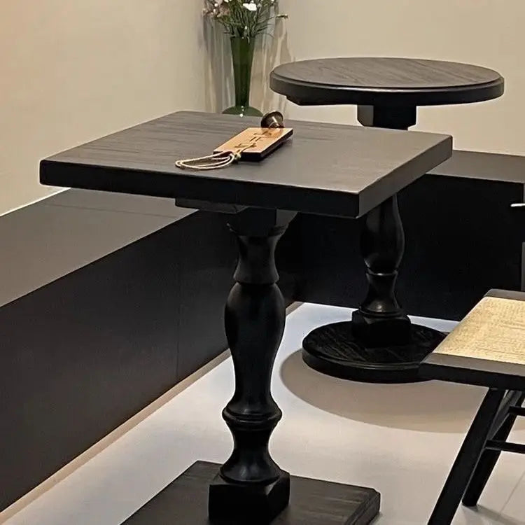 Black wooden pedestal round accent table with ornate turned legs and a square top.