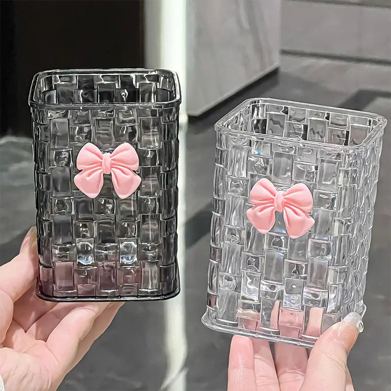 bow pen holder desktop storage organizers in clear and black translucent rectangular containers with woven cube patterns and soft pink bows.