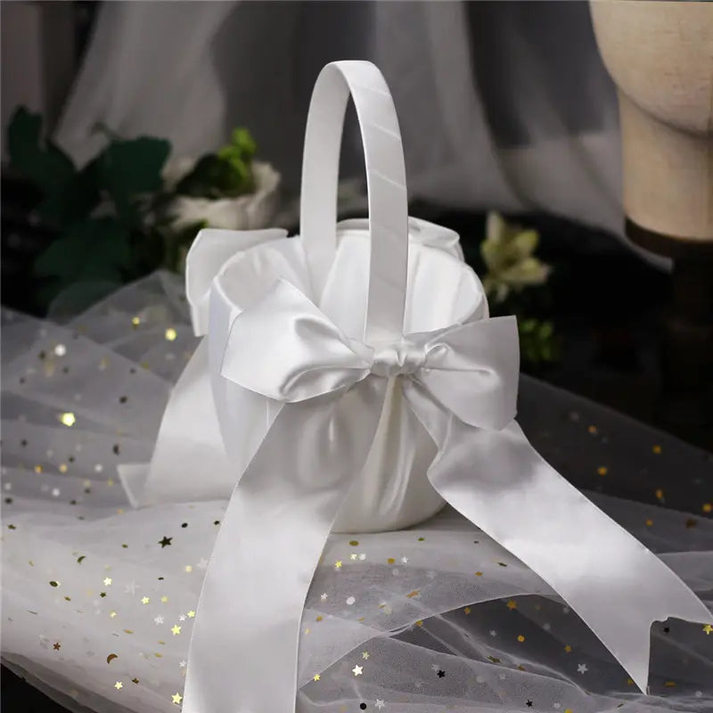 Un panier de demoiselle d’honneur en satin blanc avec une anse assortie et un grand nœud perlé noué au centre.