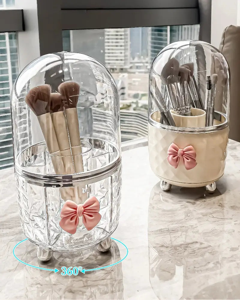 Porte-pinceaux en dôme de verre transparent, avec un accent de nœud rose et des pieds argentés, dans une boîte de rangement tournante pour maquillage et organisation des cosmétiques.