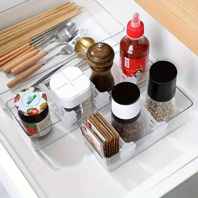 Clear plastic drawer organizer with segmented compartments holding various kitchen items featuring an adjustable refrigerator space divider made of white plastic.
