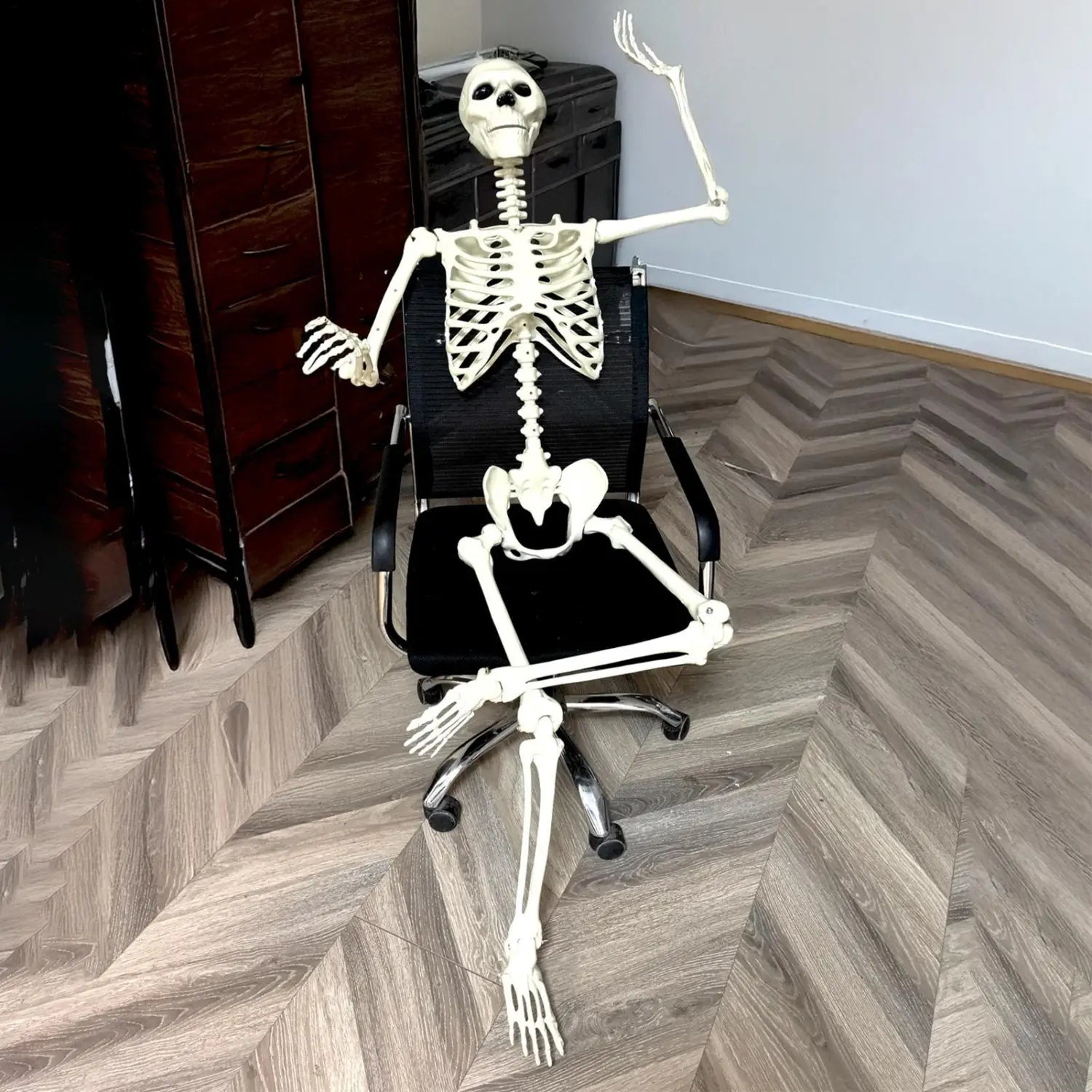 modelo de esqueleto de Halloween de plástico blanco, sentado en una silla de oficina negra, utilizado como decoración posable para exhibiciones de casa encantada