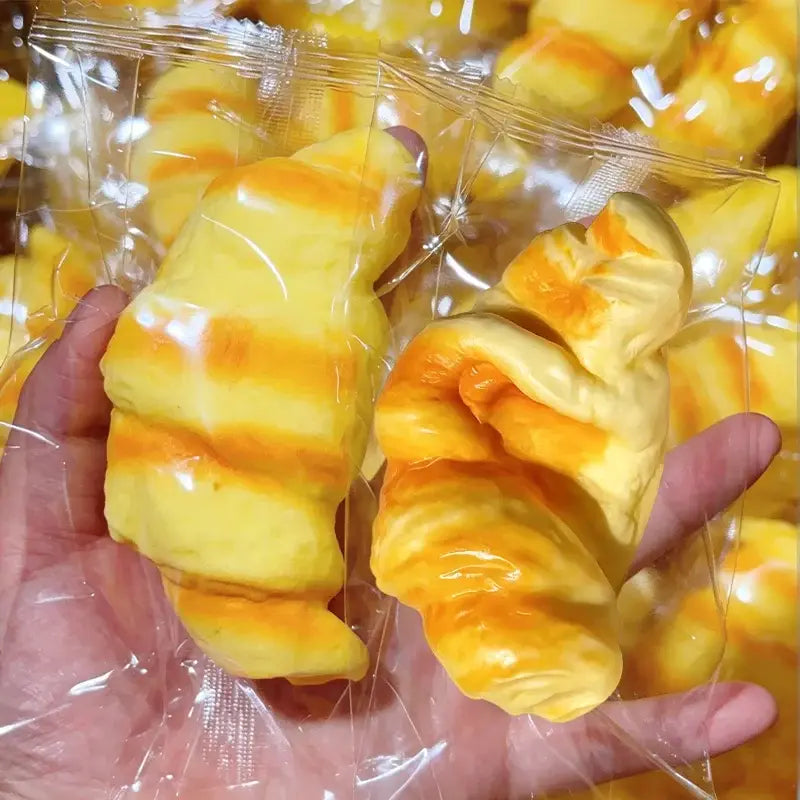 sachet en plastique transparent contenant un jouet anti-stress en forme de croissant, à bandes jaunes et orange, en forme de pain anti-stress, fabriqué en matériau souple pour un soulagement efficace du stress