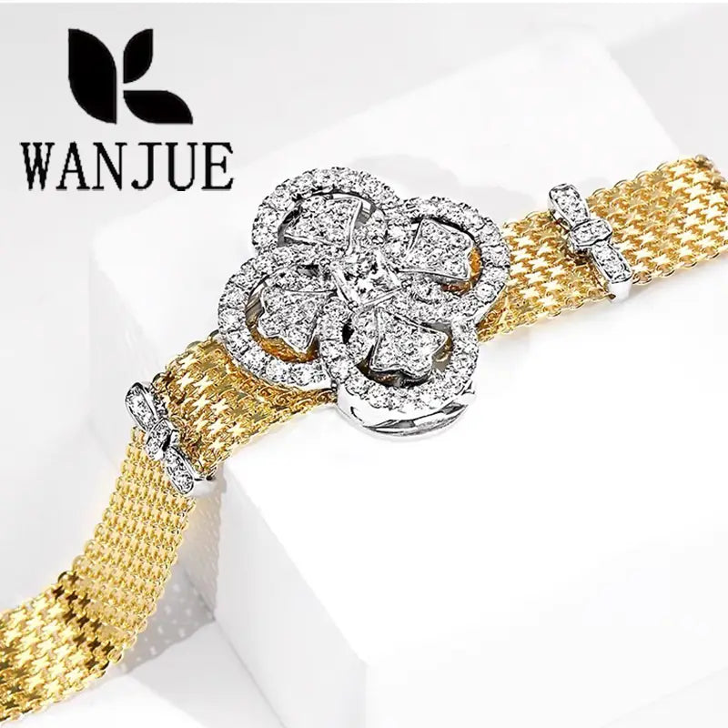 A sparkling gold mesh cuff bracelet featuring a central four-leaf clover design adorned with clear crystals and accented by smaller crystal-set bow details.