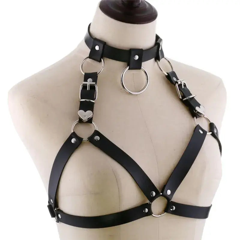 Black goth body harness made of faux leather featuring silver metal rings and heart-shaped accents as body jewelry.