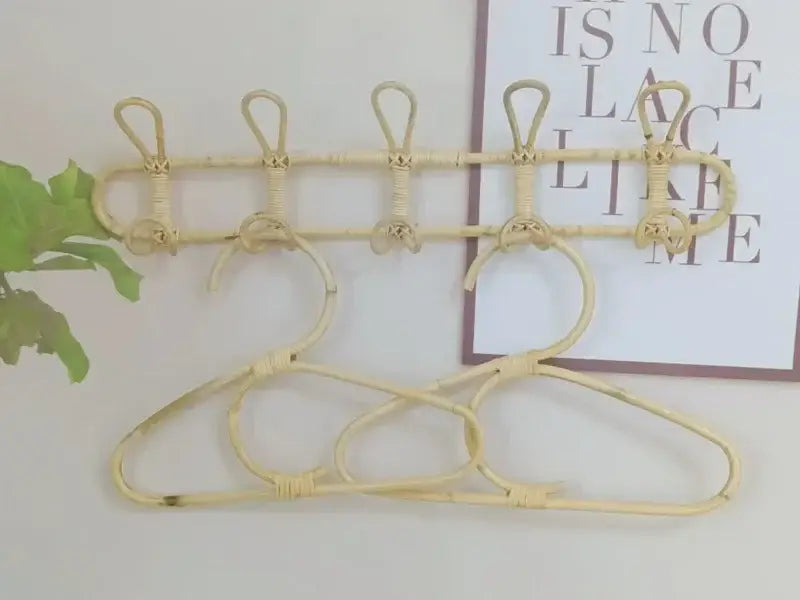 Beiger geflochtener Rattan-Kinder-Wandhaken zur Aufbewahrung von Kleidung mit fünf Haken und zwei Kleiderbügeln, an der Wand montiert.